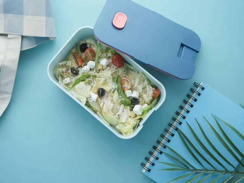 Boîte repas équilibrée et carnet de notes posés sur un plan de travail